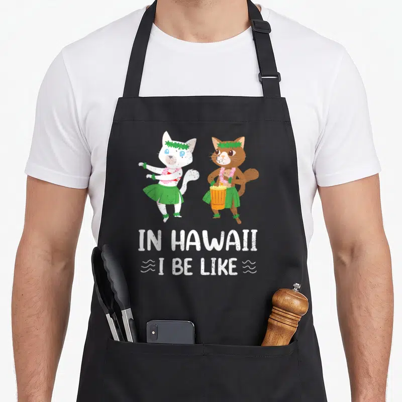 Tablier de cuisine noir avec deux chats en tenue hawaïenne et le texte In Hawaii I Be Like imprimé en blanc.