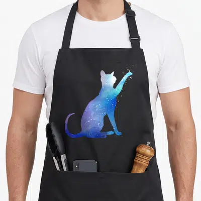 Tablier de cuisine noir avec illustration aquarelle d'un chat aux couleurs cosmiques bleues et violettes, patte avant tendue vers le haut.