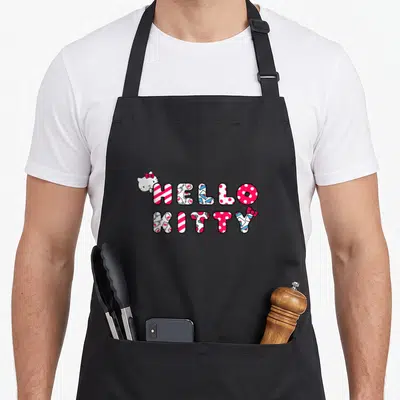 Tablier de cuisine noir avec le logo Hello Kitty en lettres colorées et un petit chat blanc à l'angle supérieur gauche.