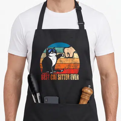 Tablier de cuisine noir avec illustration vintage d'un chat en lunettes de soleil et un poing bump sur fond arc-en-ciel dégradé.