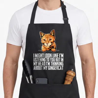 Tablier de cuisine noir avec illustration d'un chaton roux et le texte I might look like I'm listening to you but in my head I'm thinking about my gingercat