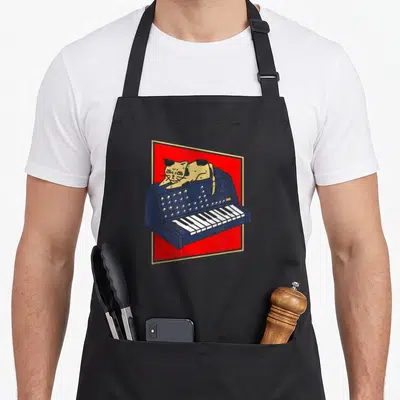 Tablier de cuisine noir avec illustration d'un chat doré posé sur un synthétiseur bleu sur fond rouge.
