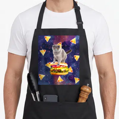 Tablier de cuisine noir avec un chat gris posant sur un burger géant entouré de nachos dans l'espace.