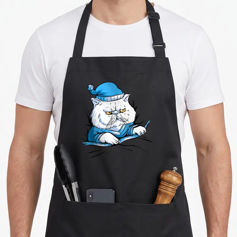 Tablier de cuisine noir avec illustration d'un chat blanc en pyjama bleu et bonnet de nuit au regard mécontent.