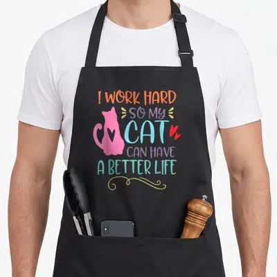Tablier de cuisine noir avec une silhouette de chat rose et un texte coloré humoristique sur le devant.