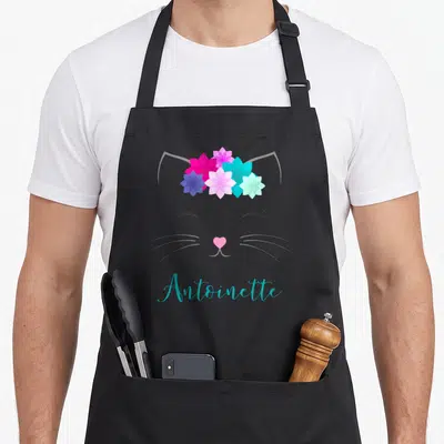 Tablier de cuisine noir avec illustration de chat aux fleurs et le nom Antoinette en bleu turquoise.