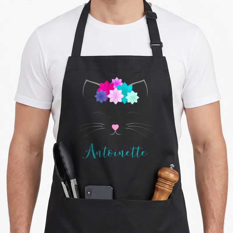 Tablier de cuisine noir avec illustration de chat aux fleurs et le nom Antoinette en bleu turquoise.