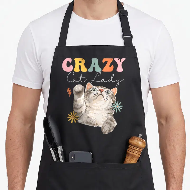 Tablier de cuisine noir avec illustration rétro d'un chat tigré jouant avec des fleurs et le texte CRAZY Cat Lady Groovy.