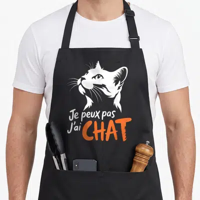 Tablier de cuisine noir avec illustration tête de chat blanc et texte Je peux pas J'ai CHAT en orange.