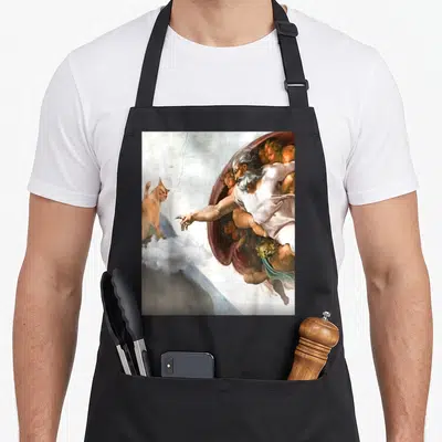 Tablier de cuisine noir avec une parodie de la Création de Michel-Ange montrant un chat orange sur un nuage.