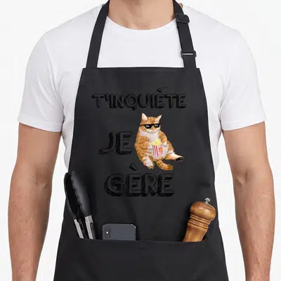 Tablier de cuisine noir avec un chat aux lunettes pixel tenant du popcorn et le texte T'inquiète Je Gère.