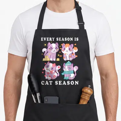Tablier de cuisine noir avec quatre chatons colorés représentant les saisons et le texte Every Season Is Cat Season.