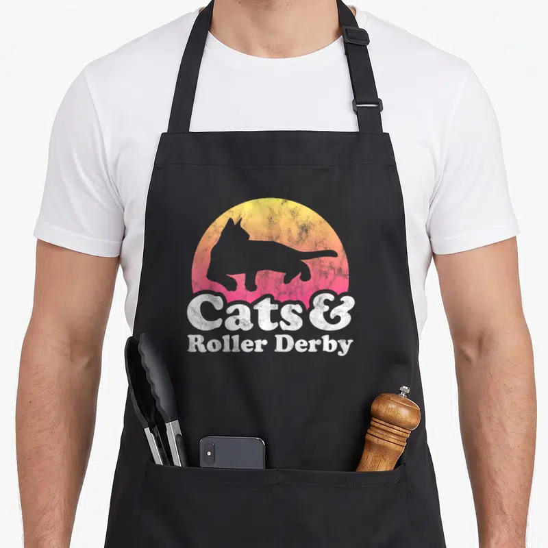Tablier de cuisine noir avec silhouette de chat sur fond dégradé et texte Cats & Roller Derby en blanc.
