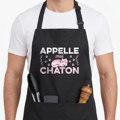 Tablier de cuisine noir avec un chaton rose, des traces de pattes et le texte Appelle moi Chaton en blanc et rose.