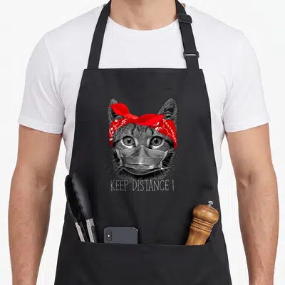 Tablier de cuisine noir avec illustration de chat portant un masque et un bandana rouge.