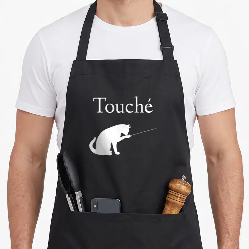 Tablier de cuisine noir avec silhouette blanche de chat tenant une épée et le mot Touché.