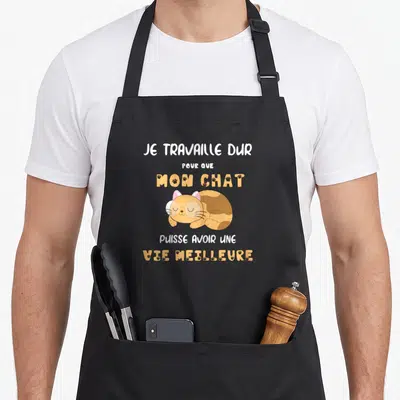 Tablier de cuisine noir avec un chat doré dormant et un message humoristique sur le travail pour lui offrir une meilleure existence.
