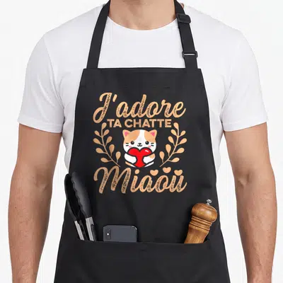 Tablier de cuisine noir avec illustration d'un chaton tricolore tenant un cœur rouge entouré de texte orange