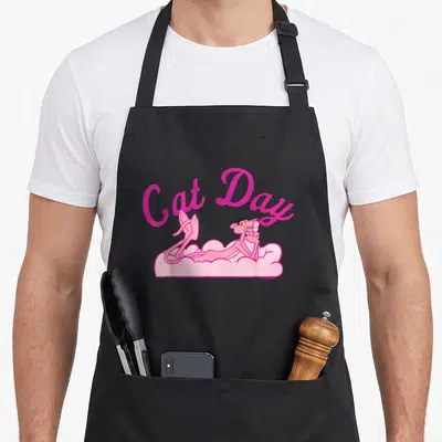 Tablier de cuisine noir avec la Panthère rose allongée sur un nuage et le texte Cat Day.