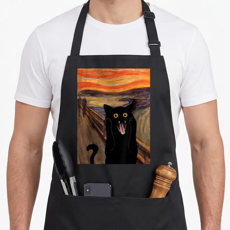 Tablier de cuisine noir avec un chat noir parodiant Le Cri de Munch sur fond orange et violet.