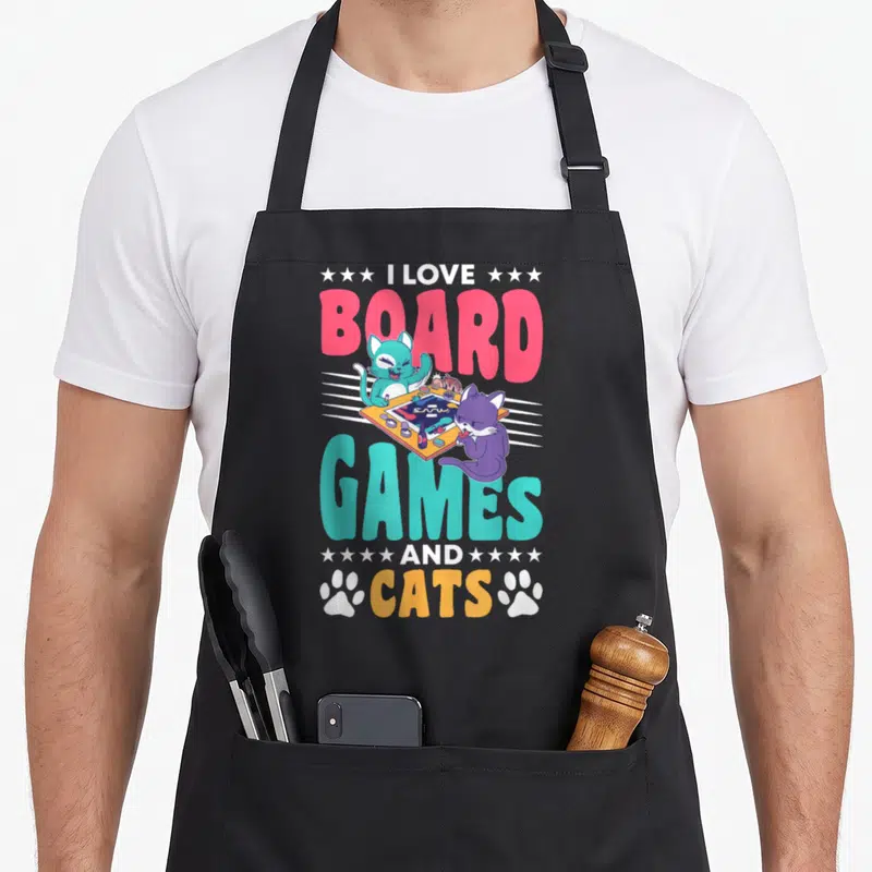 Tablier de cuisine noir avec deux chats jouant à un jeu de société entourés du texte I Love Board Games and Cats.