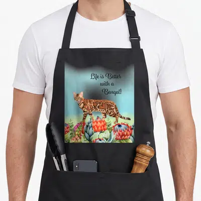 Tablier de cuisine noir avec illustration d'un chat Bengal et fleurs exotiques sur fond bleu clair.