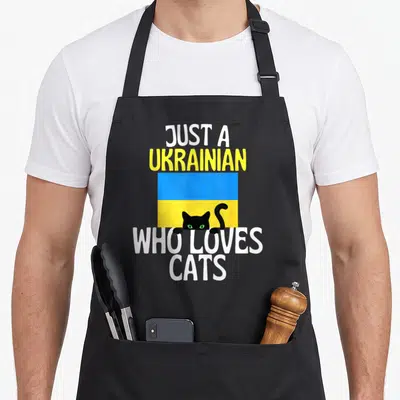 Tablier de cuisine noir avec drapeau ukrainien et tête de chat noir aux yeux verts.