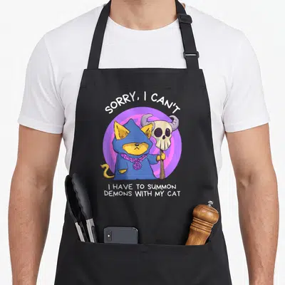 Tablier de cuisine noir avec un chat en sorcier bleu tenant une staffe à tête de mort sur fond violet.