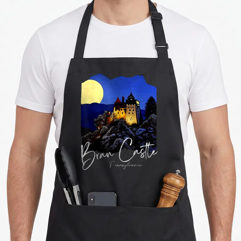 Tablier de cuisine noir avec illustration du Château de Bran et texte Bran Castle Transylvania en blanc.