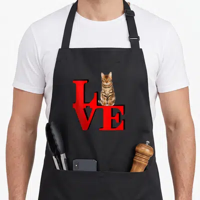 Tablier de cuisine noir avec inscription Love rouge et illustration de chat Bengal assis sur les lettres.