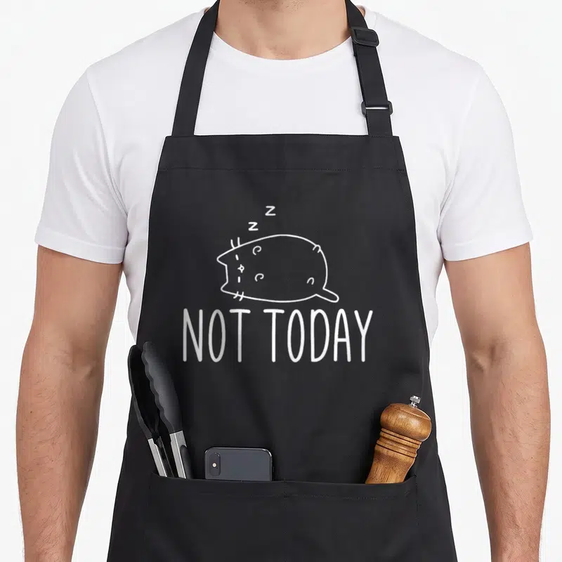 Tablier de cuisine noir avec un dessin blanc représentant un chat rond dormant et le texte Not Today.