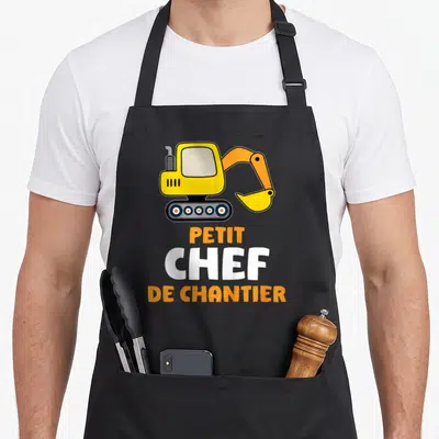 Tablier de cuisine noir avec illustration de tractopelle jaune et texte Petit Chef De Chantier en orange et blanc.