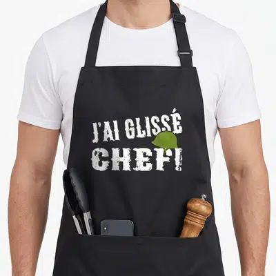 Tablier de cuisine noir avec l'inscription J'ai glissé chef et un casque militaire vert posé sur les lettres.