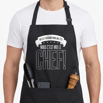 Tablier de cuisine noir avec inscription blanche On est plusieurs dans ma tête mais c'est moi le chef et une bannière décorative.