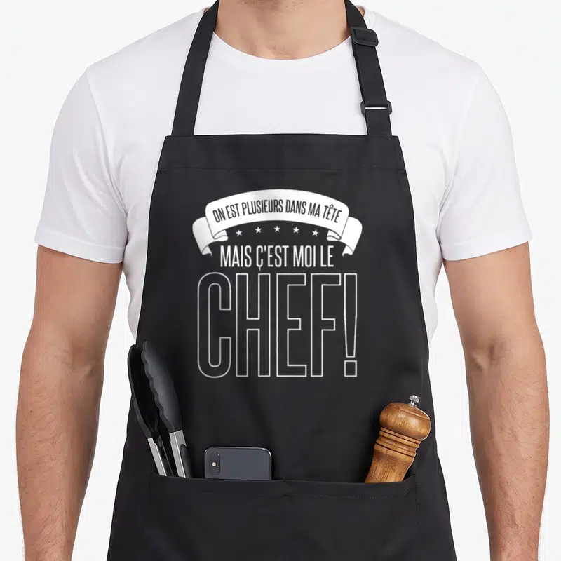 Tablier de cuisine noir avec inscription blanche On est plusieurs dans ma tête mais c'est moi le chef et une bannière décorative.