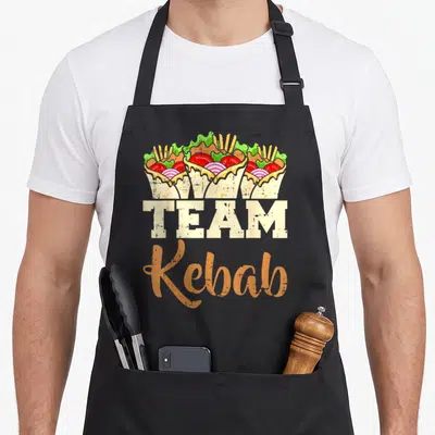 Tablier de cuisine noir avec trois doners colorés et le texte TEAM Kebab en typographie vintage beige et orange.