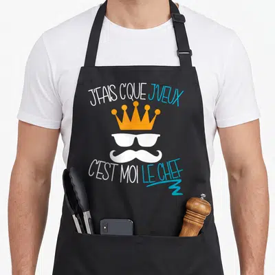Tablier de cuisine noir avec couronne orange, lunettes blanches, moustache et texte j'fais c'que je veux c'est moi le chef