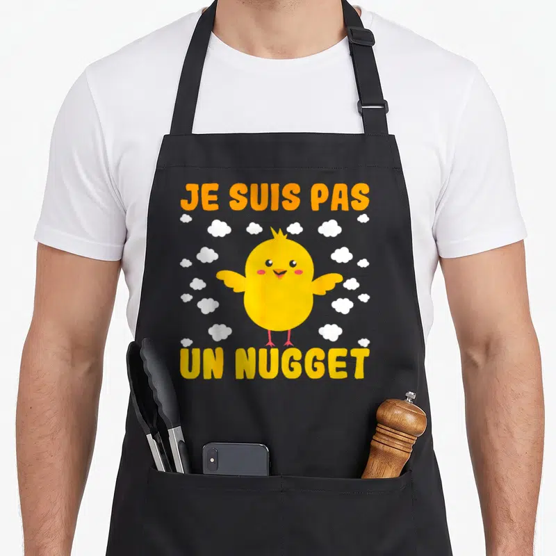 Tablier de cuisine noir avec poussin jaune et texte Je suis pas un nugget entouré de nuages blancs.