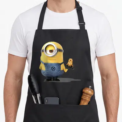 Tablier de cuisine noir avec un Minion jaune à l'oeil unique tenant un biscuit en forme de petit robot doré.