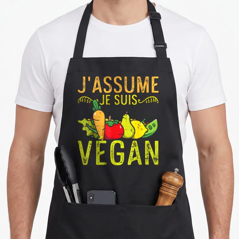Tablier de cuisine noir avec inscription J'assume je suis végan et légumes souriants colorés sur le devant.