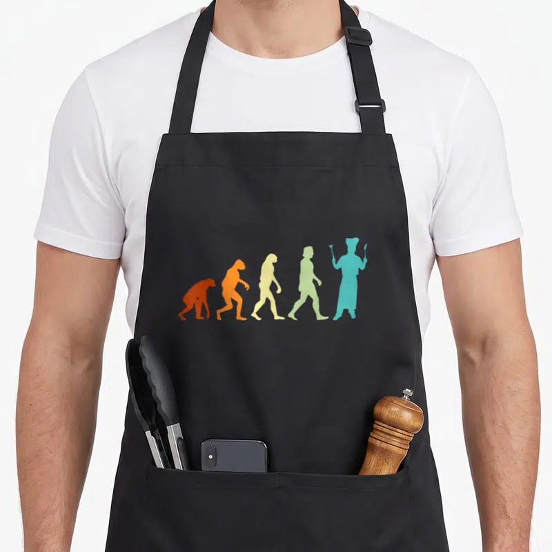 Tablier de cuisine noir avec silhouettes colorées représentant l'évolution vers un chef tenant ustensiles