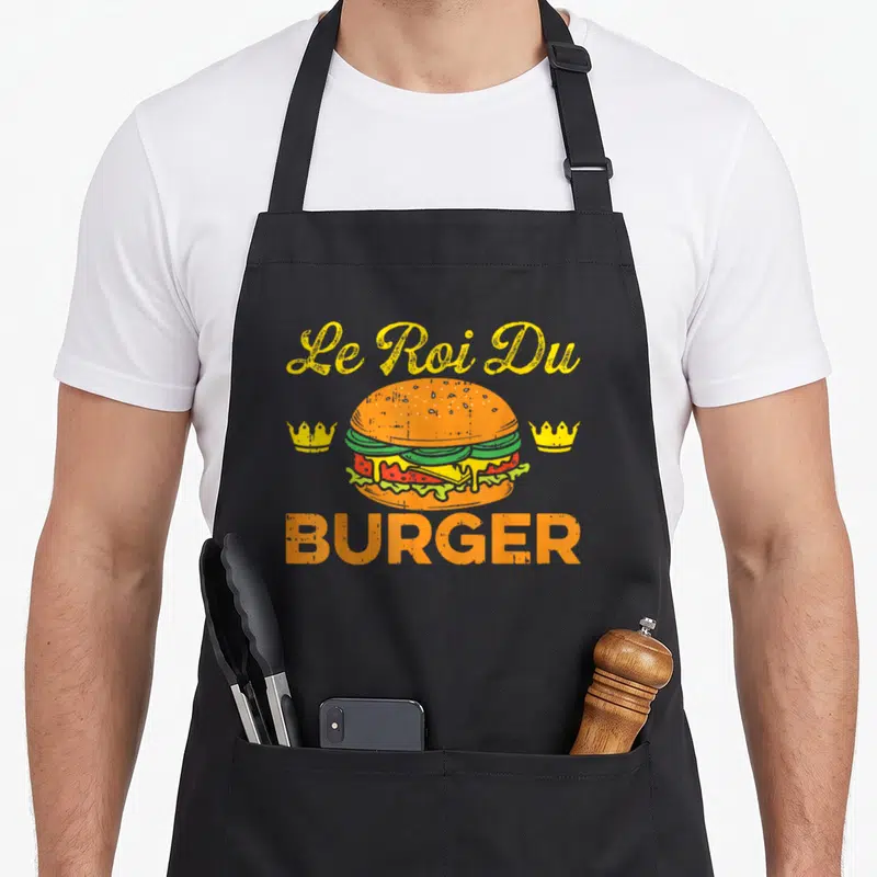 Tablier de cuisine noir avec illustration d'un burger et texte Le Roi Du Burger en jaune et orange.