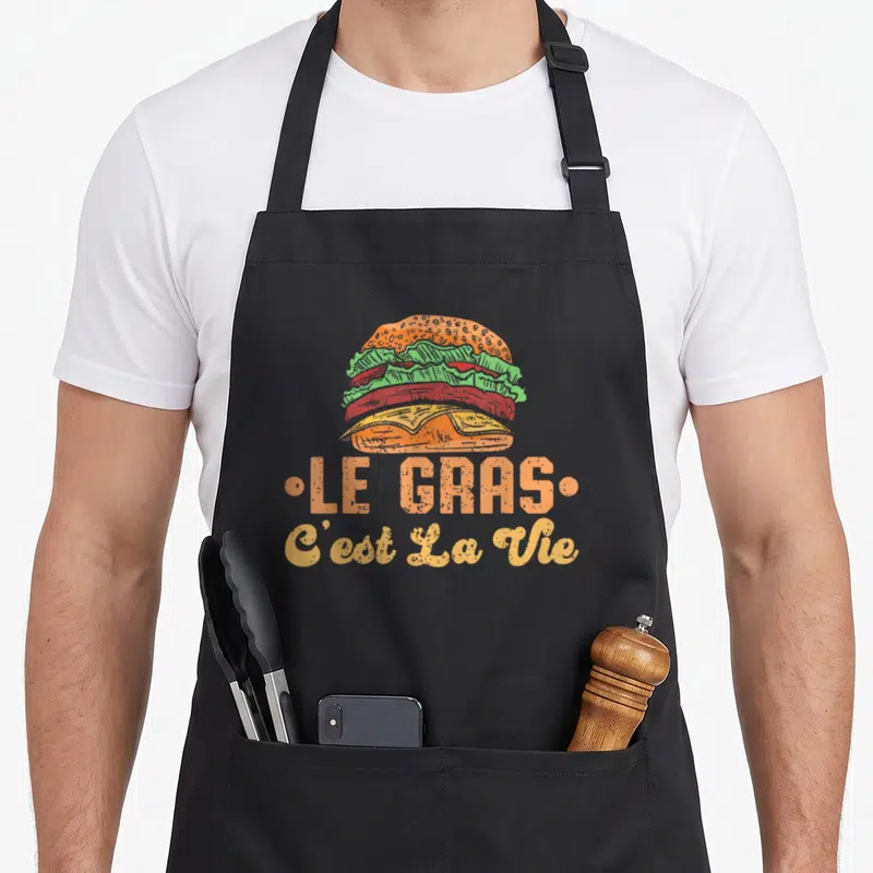 Tablier de cuisine noir avec illustration de burger colorée et texte Le Gras Cest La Vie en orange et jaune.