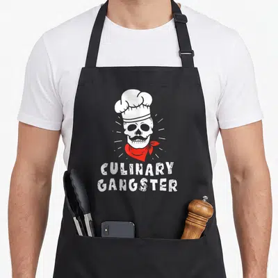 Tablier de cuisine noir avec illustration d'un crâne portant une toque blanche et un foulard rouge sous le texte culinaire Gangster.
