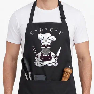 Tablier de cuisine noir avec illustration d'un crâne de cuisinier barbu tenant couteau et fourchette.