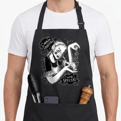 Tablier de cuisine noir avec illustration d'une sorcière versant des paillettes depuis un flacon magique.
