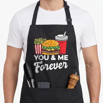 Tablier de cuisine noir avec illustration de burger, frites et boisson rouge sous le texte You & Me Forever en blanc.