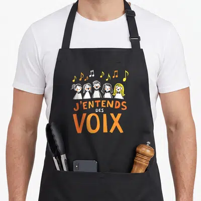 Tablier de cuisine noir avec illustration d'une chorale d'enfants et texte J'entends des voix en orange.