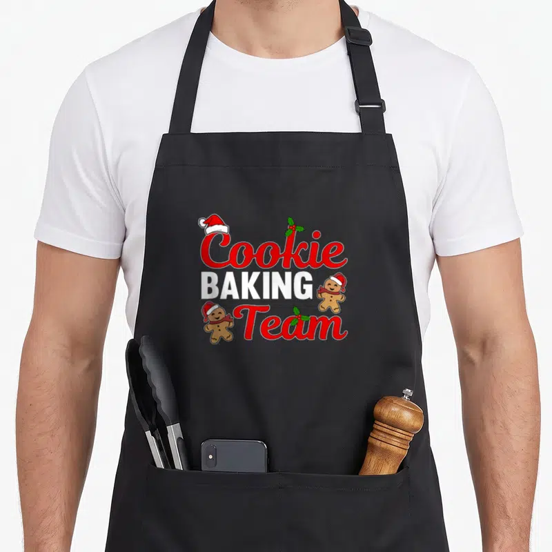 Tablier de cuisine noir avec linscription Cookie Baking Team, bonshommes en pain d'épice et décorations de Noël rouges et vertes.