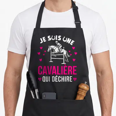 Tablier de cuisine noir avec illustration cavalière sautant un obstacle et texte Je suis une cavalière qui déchire entouré de cœurs roses.
